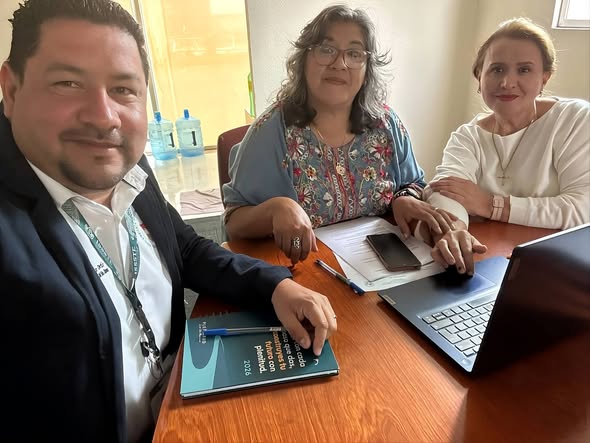 Tres integrantes de la Sección XIX reunidos alrededor de una mesa con documentos en una oficina.